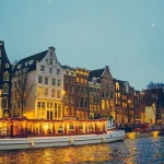 boat sailing on river near lighted houses and trees